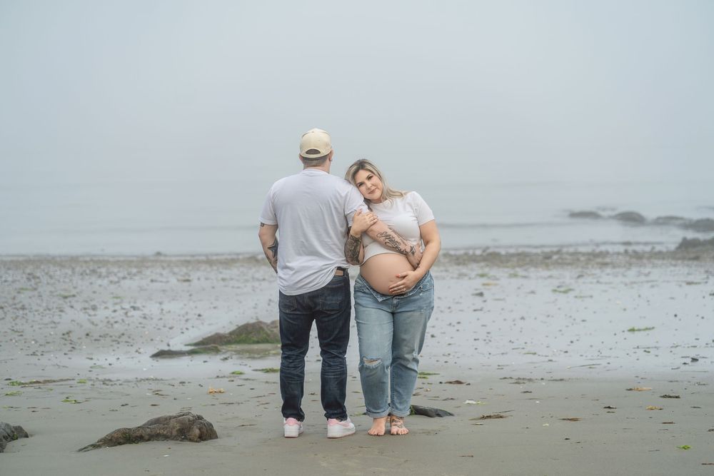 A couple stands on a misty beach at sunset holding hands and walking along the shoreline.