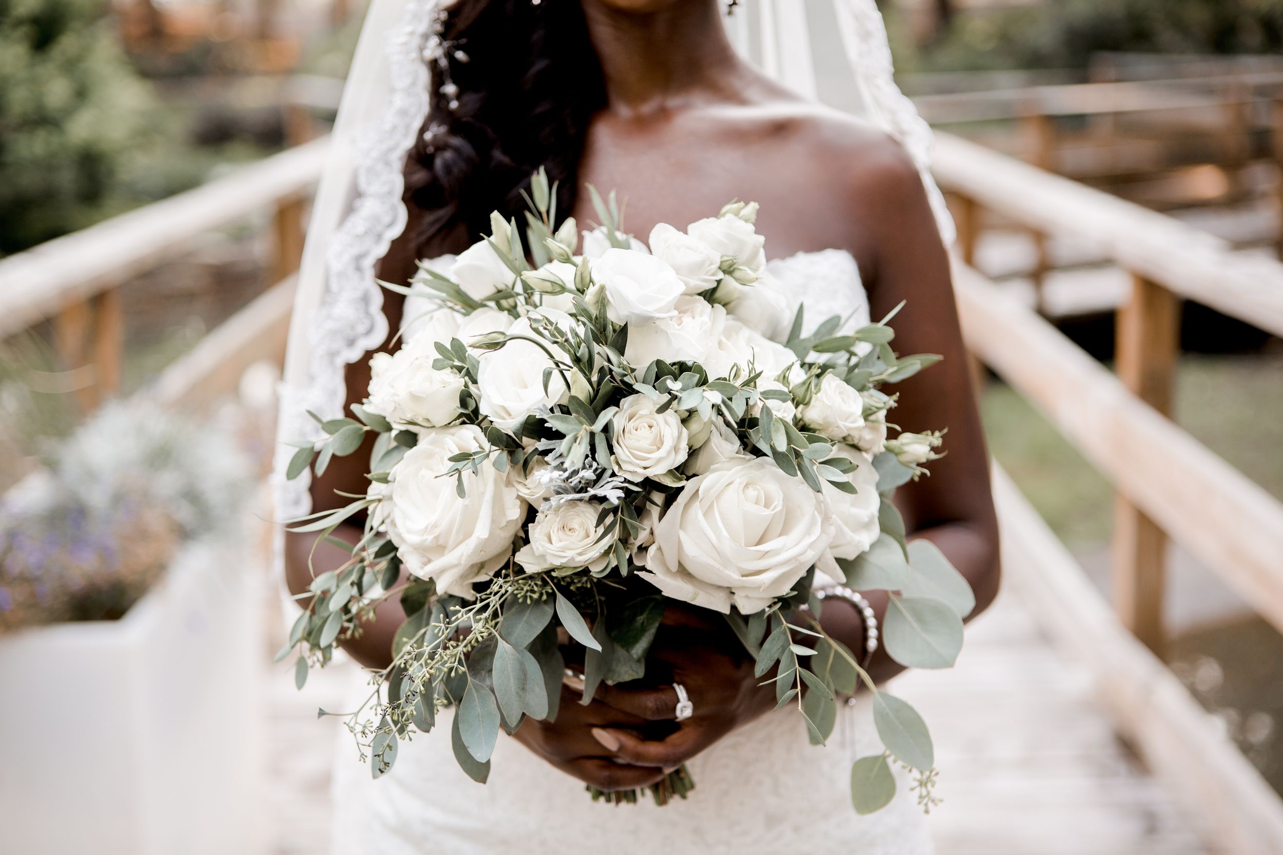 Elegant white bridal bouquet with roses and eucalyptus leaves held against a light background.