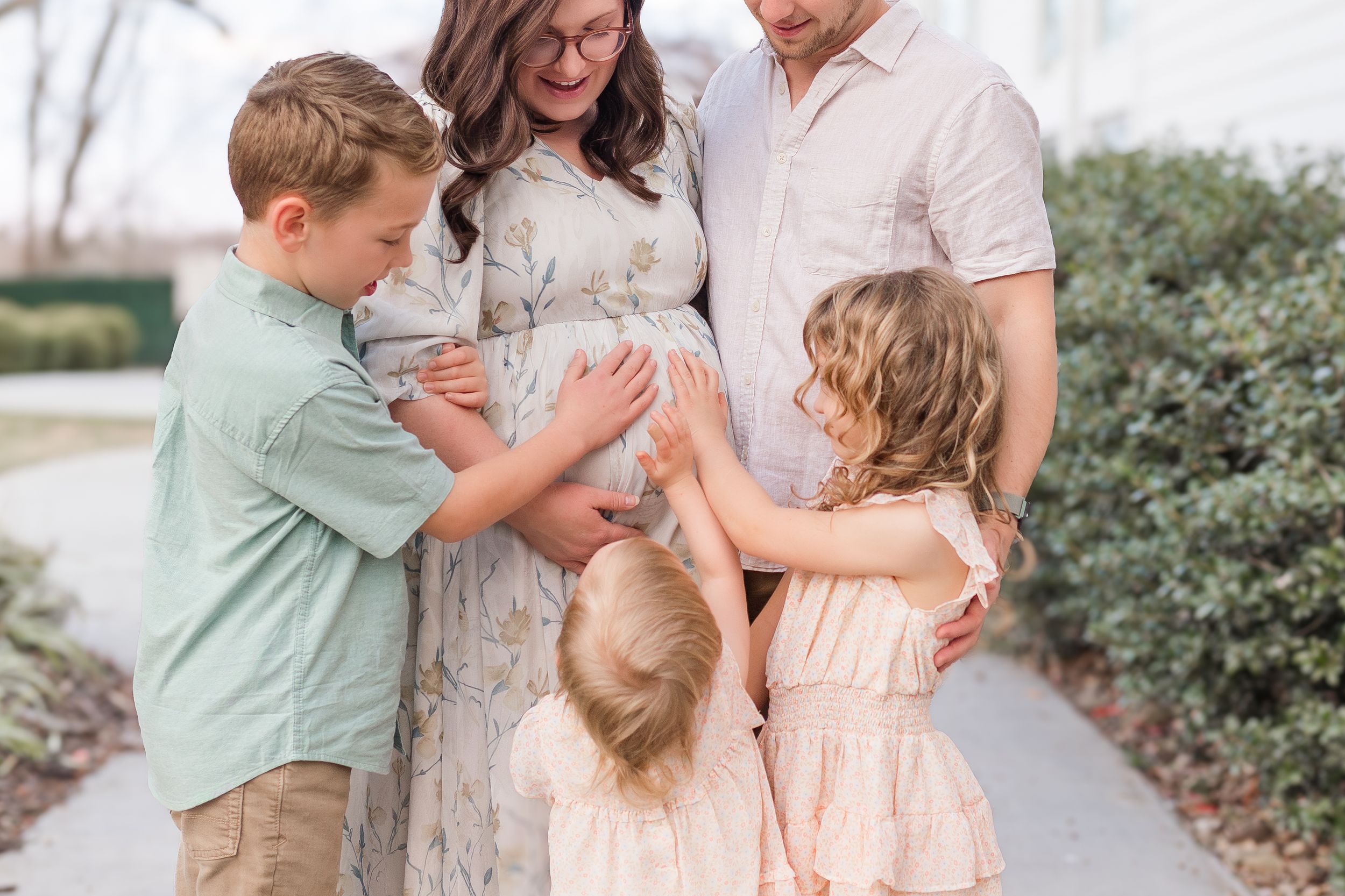 Expectant parents smiling with their three children gathered around the mother's baby bump during an outdoor family maternity session.