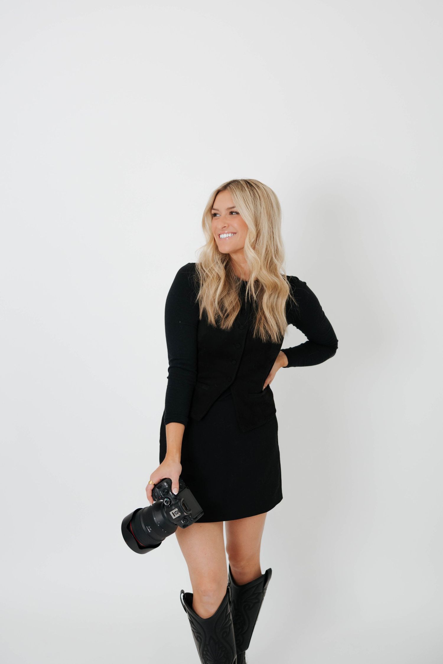 Photographer in black sweater and boots poses playfully against white background in fashion photo series in Rockford, MI