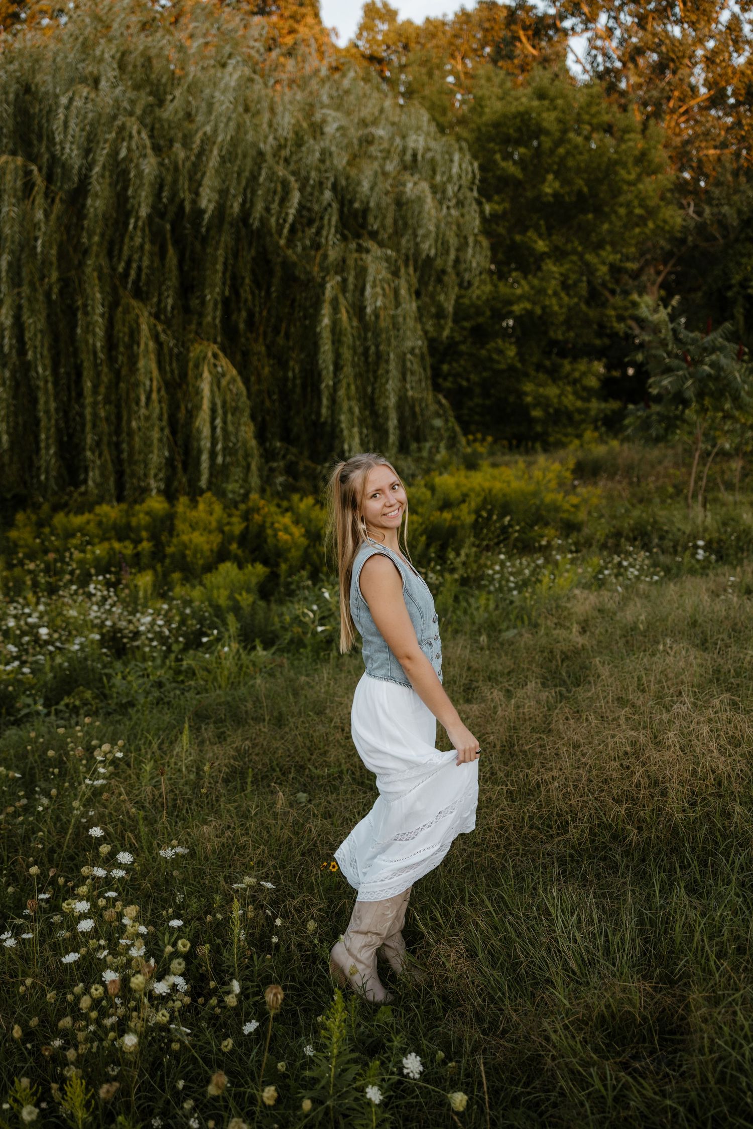 A young woman stands in a lush garden surrounded by trees and wildflowers on a sunny day. Fort Worth Texas photographer.