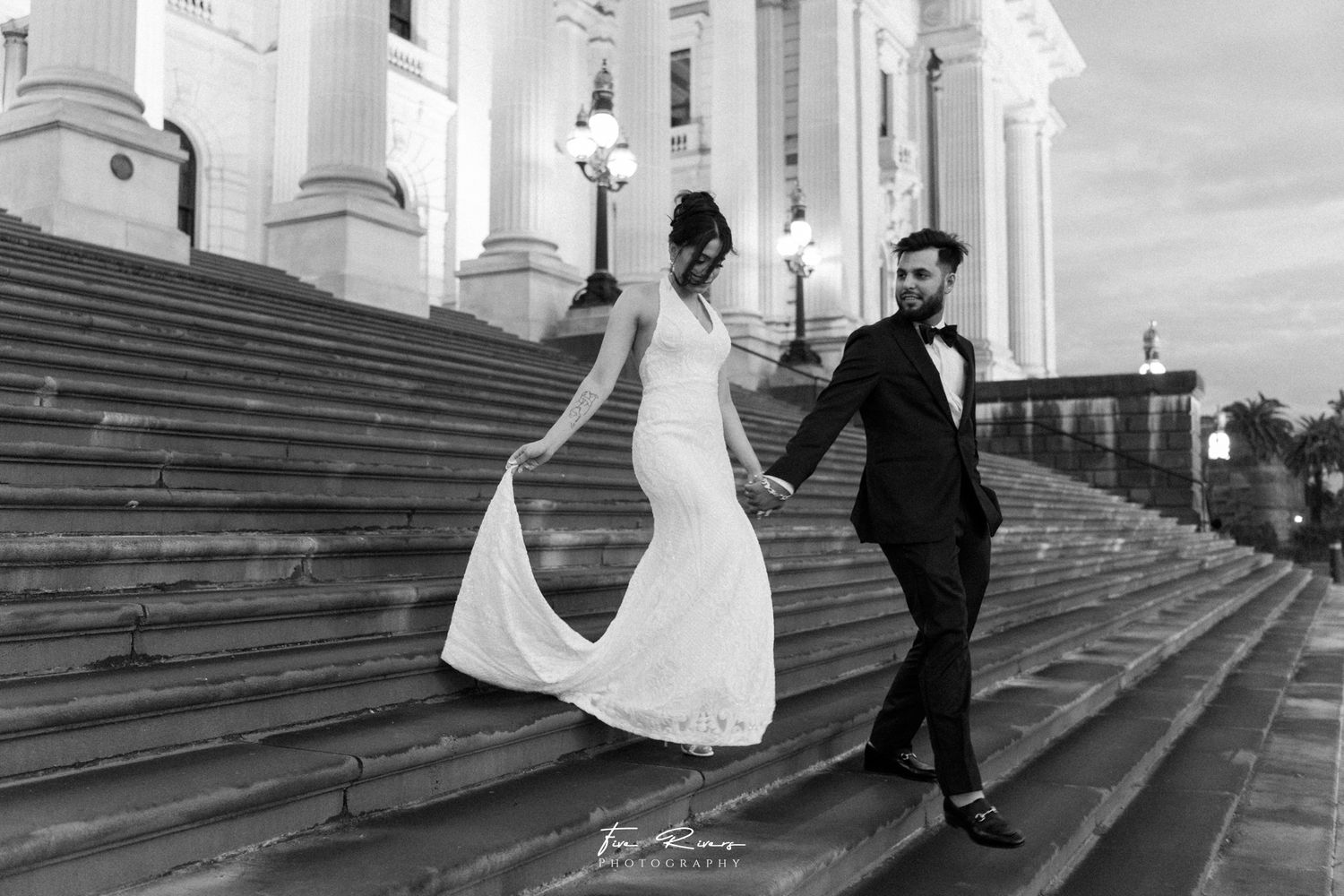 A romantic black and white moment captured on grand stone steps with elegant columns in the background.