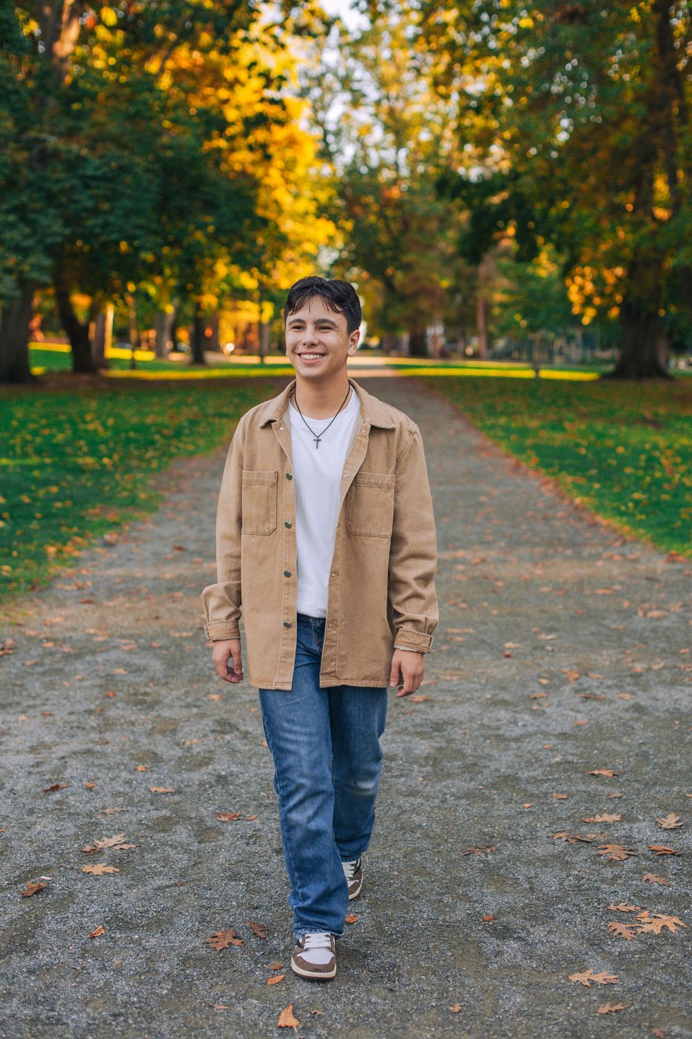 Person in casual tan jacket walking along tree-lined path with fall foliage. Spokane Liberty Lake Photographer Senior Photographer