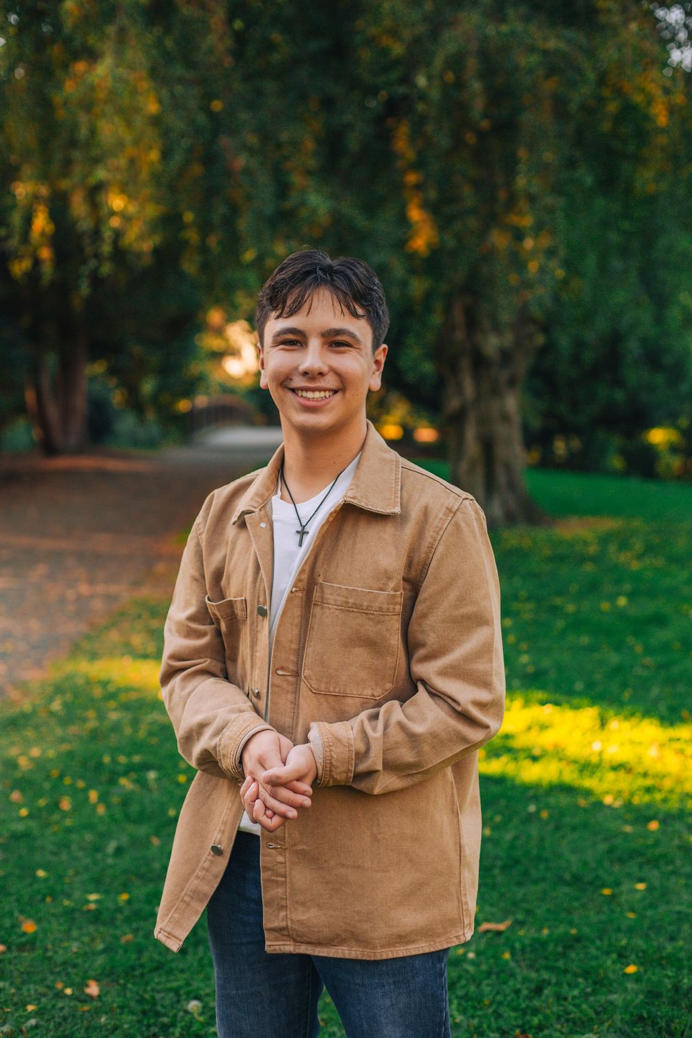 Person in tan jacket smiling outdoors with autumn trees in background. Spokane Liberty Lake Photographer Senior Photographer