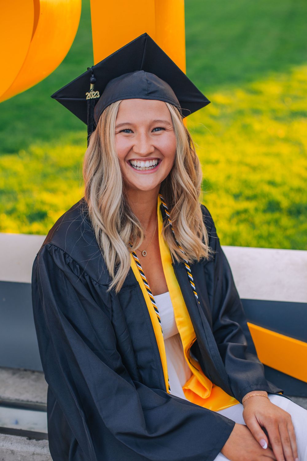 Graduate in cap and gown with yellow stole smiling against orange background. Spokane Liberty Lake Photographer Senior Photographer
