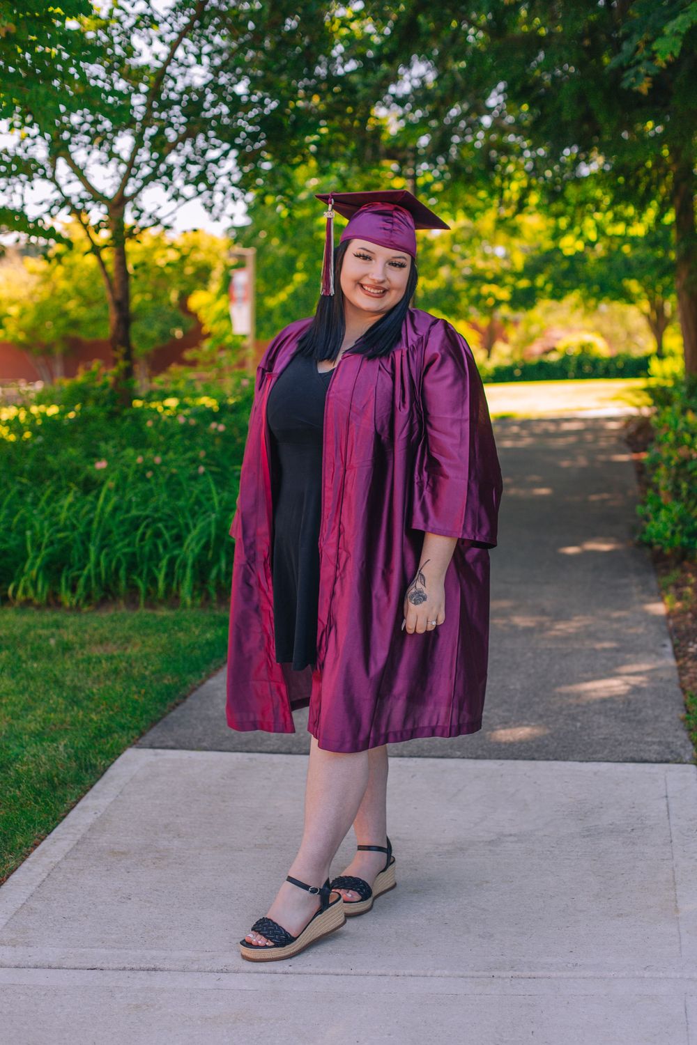 Graduate in purple cap and gown poses on concrete path surrounded by greenery. Fedore Photography Spokane Liberty Lake Photographer Senior P