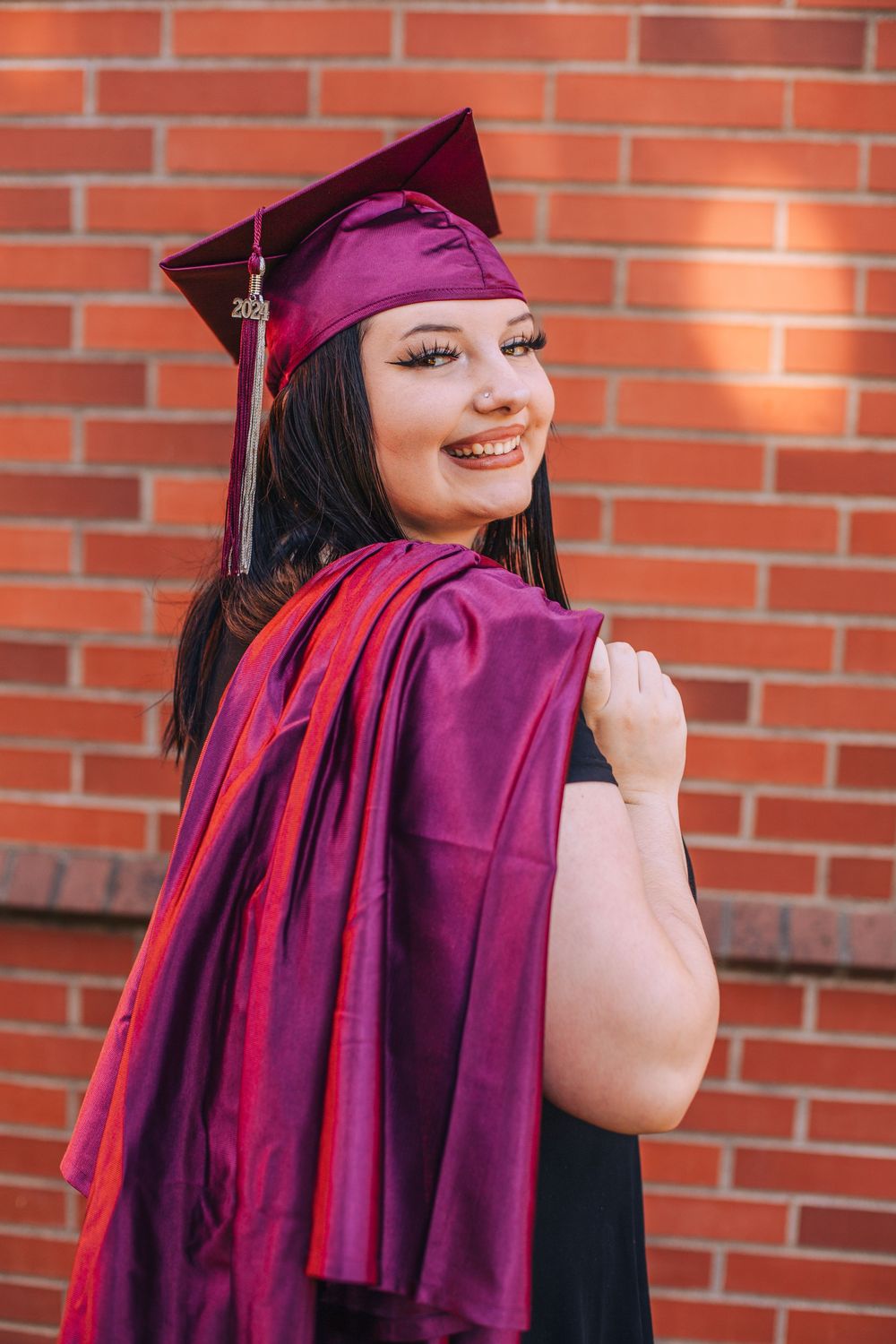 Close-up of graduate in purple academic regalia posing against red brick wall. Fedore Photography Spokane Liberty Lake Photographer Senior