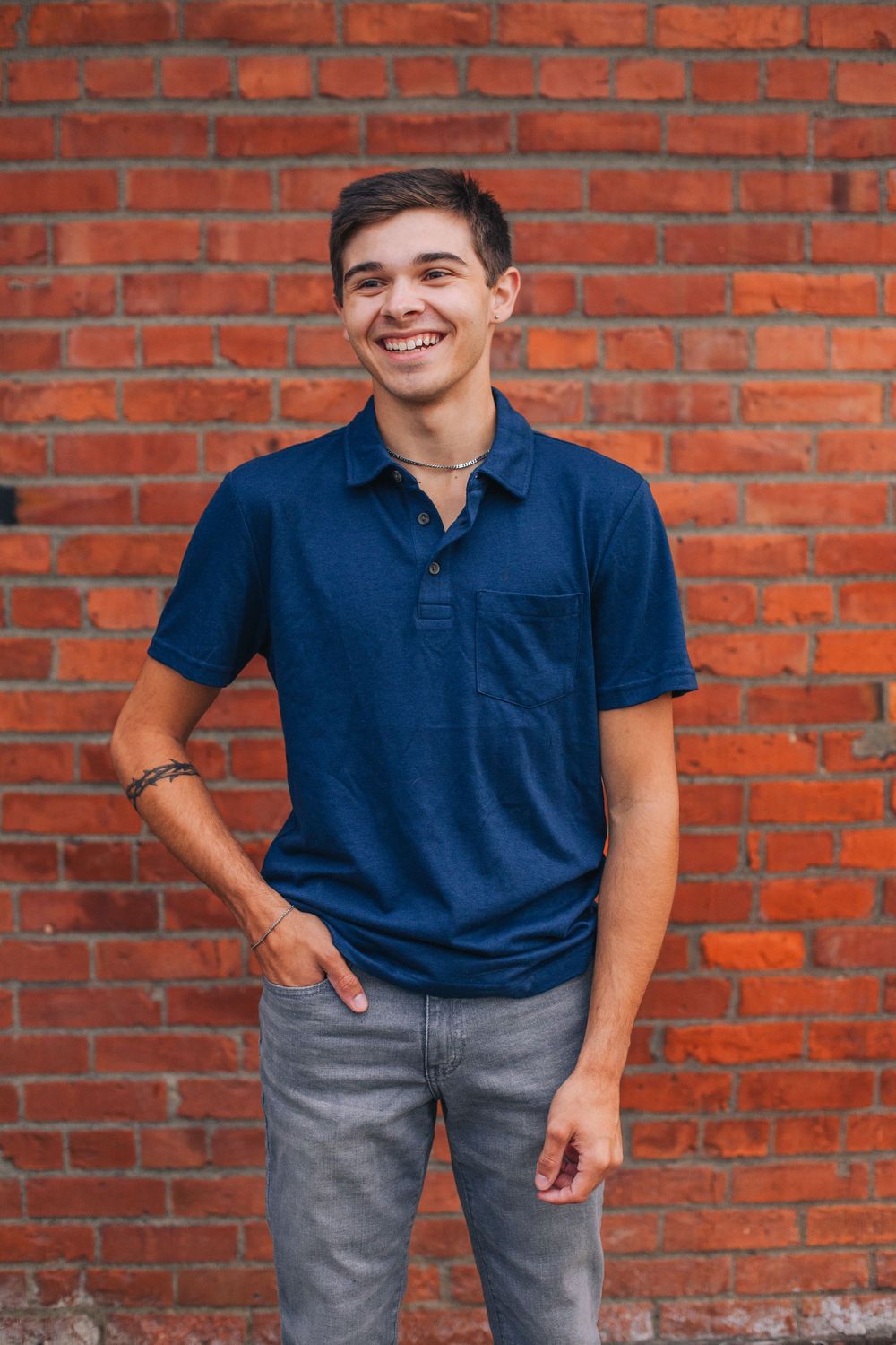 Athletic person in navy polo and gray pants poses against rustic brick wall. Spokane Liberty Lake Photographer Senior Photographer