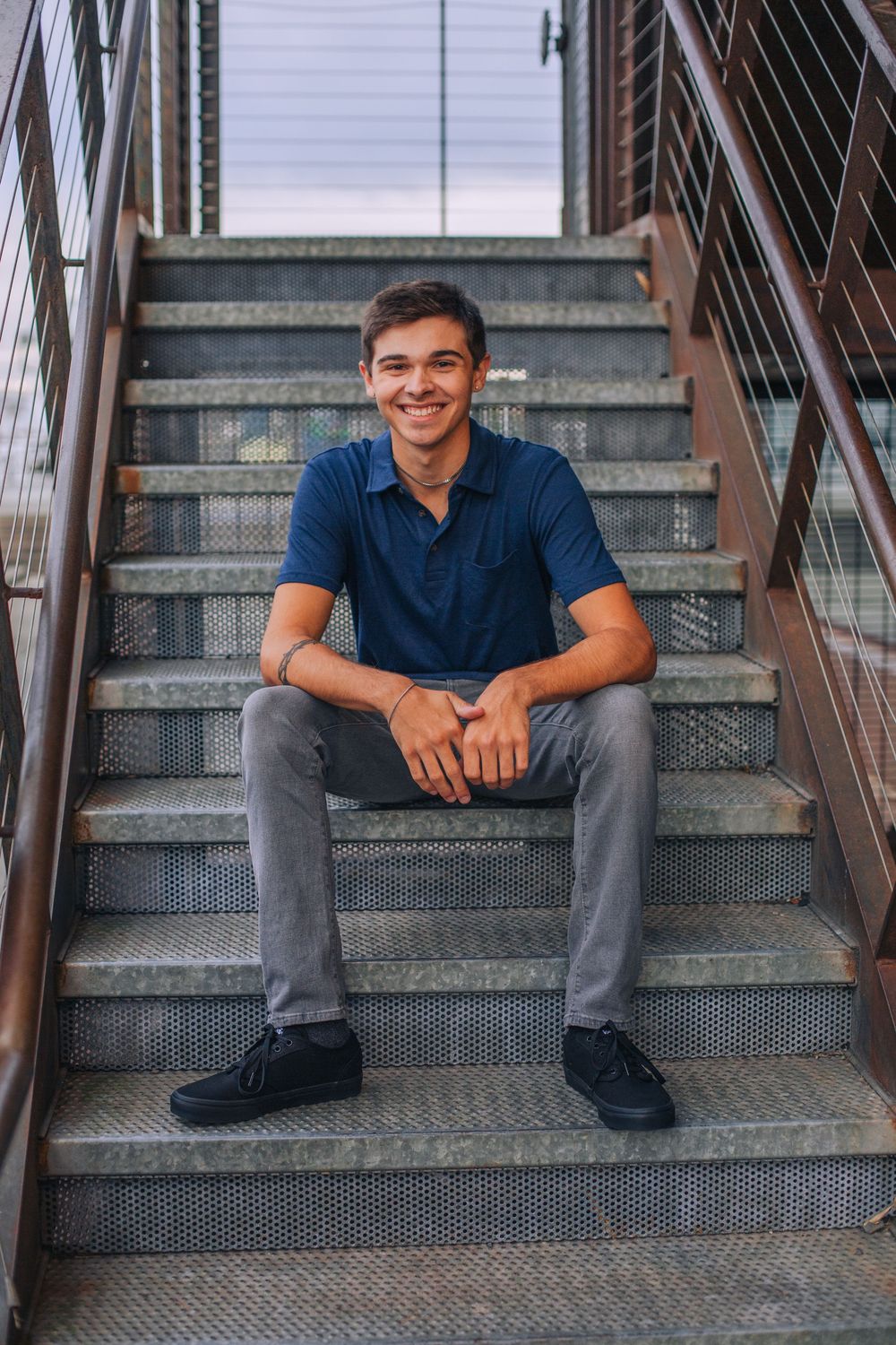 Person in blue polo shirt sitting casually on industrial metal stairs. Spokane Liberty Lake Photographer Senior Photographer