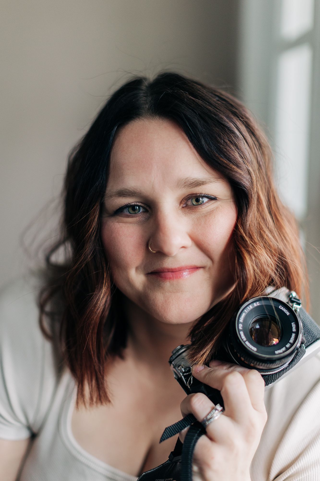 A photographer in a cream-colored top smiles while holding a vintage camera.