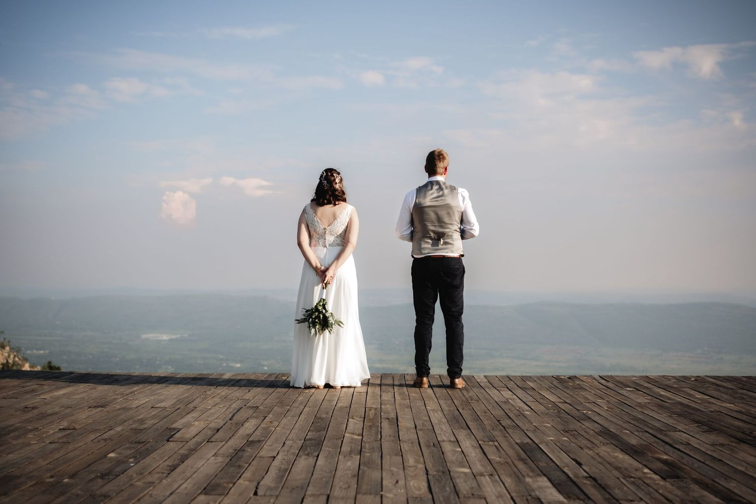 A couple stands on a wooden deck overlooking misty mountains on their wedding day. Photos by Wouter Kleynhans at Intiem Weddings