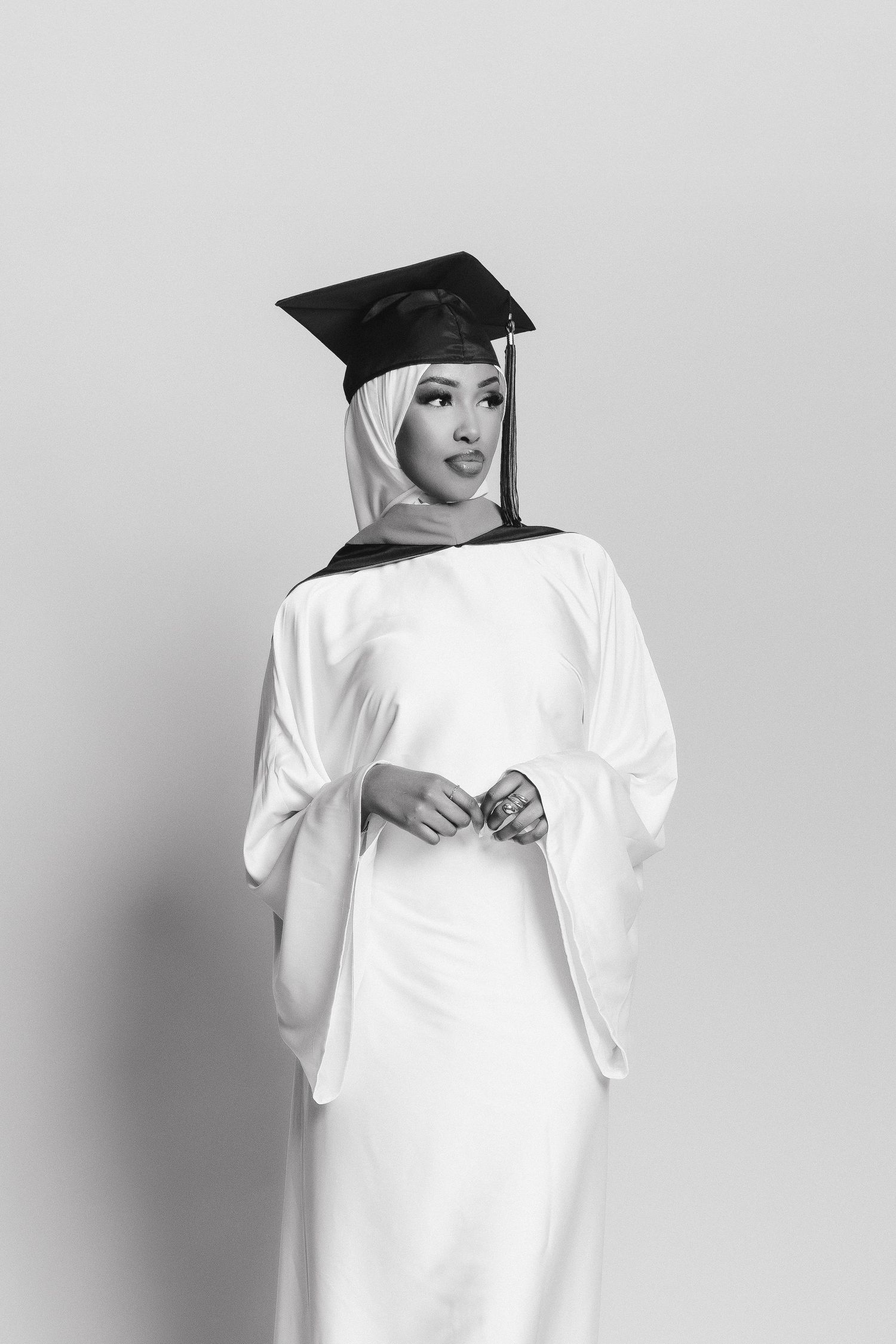 Graduate in white dress and cap poses against light background.