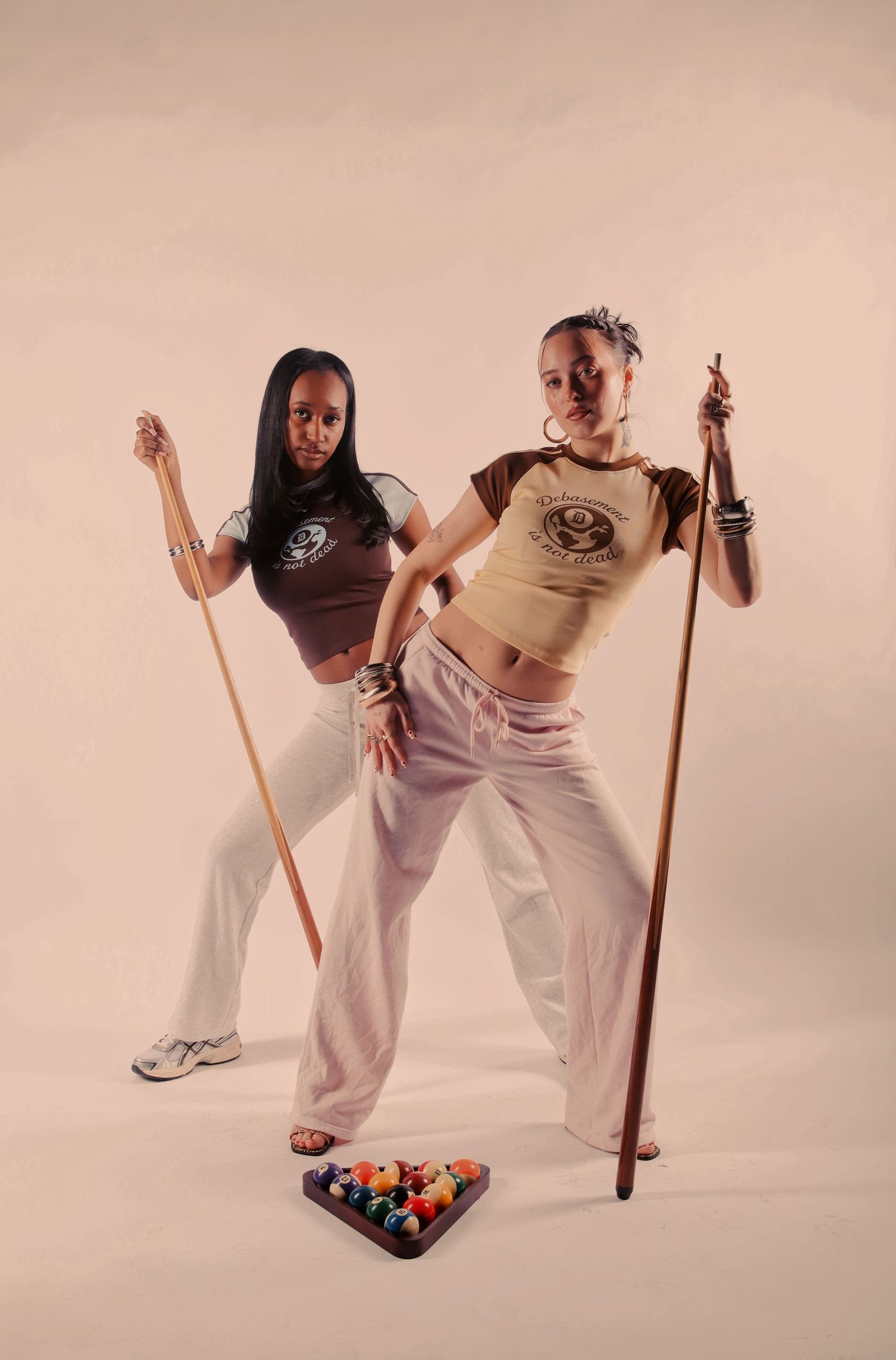 Someone in casual sportswear with chunky sneakers sits posed against a beige studio backdrop.