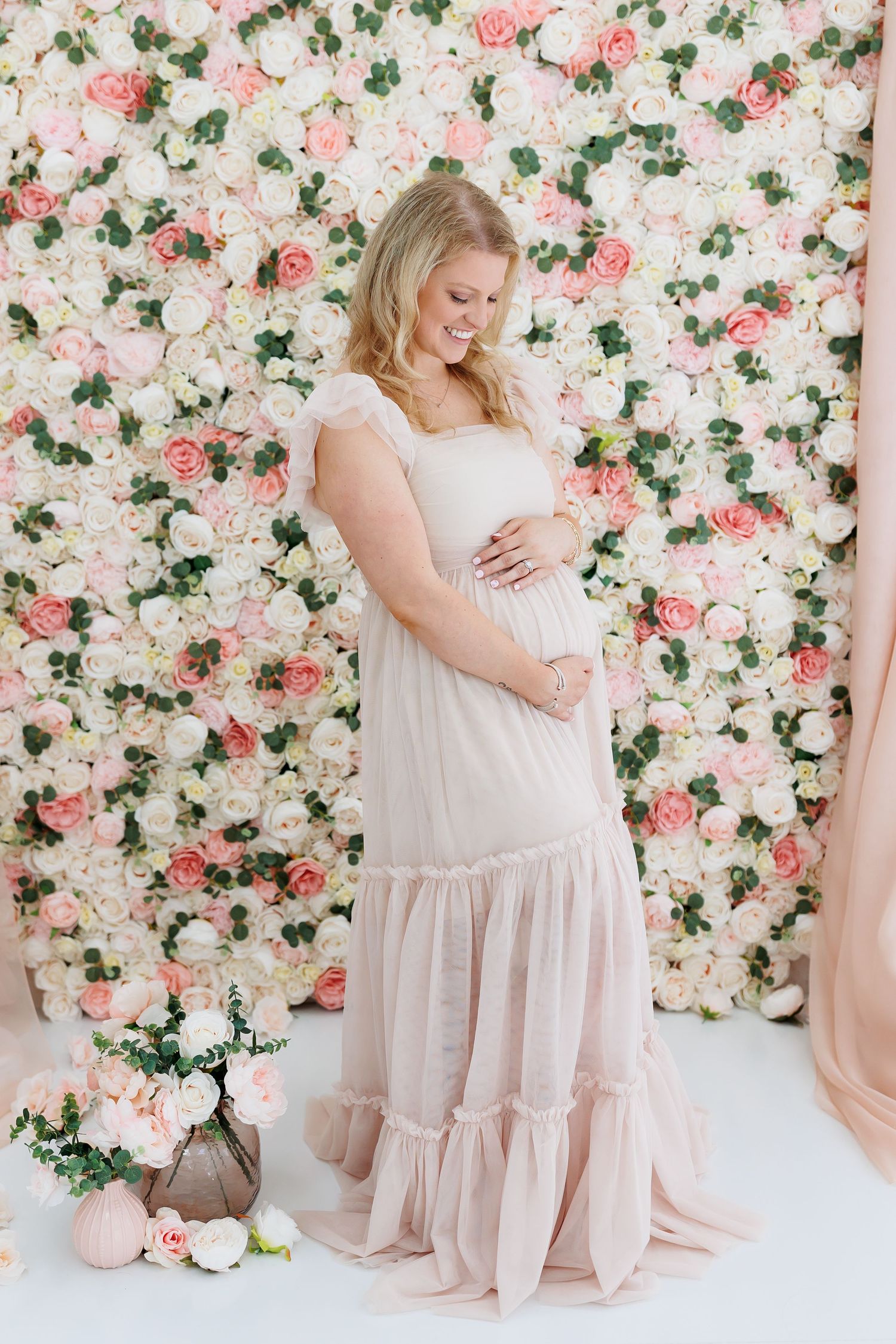 Maternity photo against floral backdrop with pink and white roses featuring an ethereal blush tiered maxi dress.