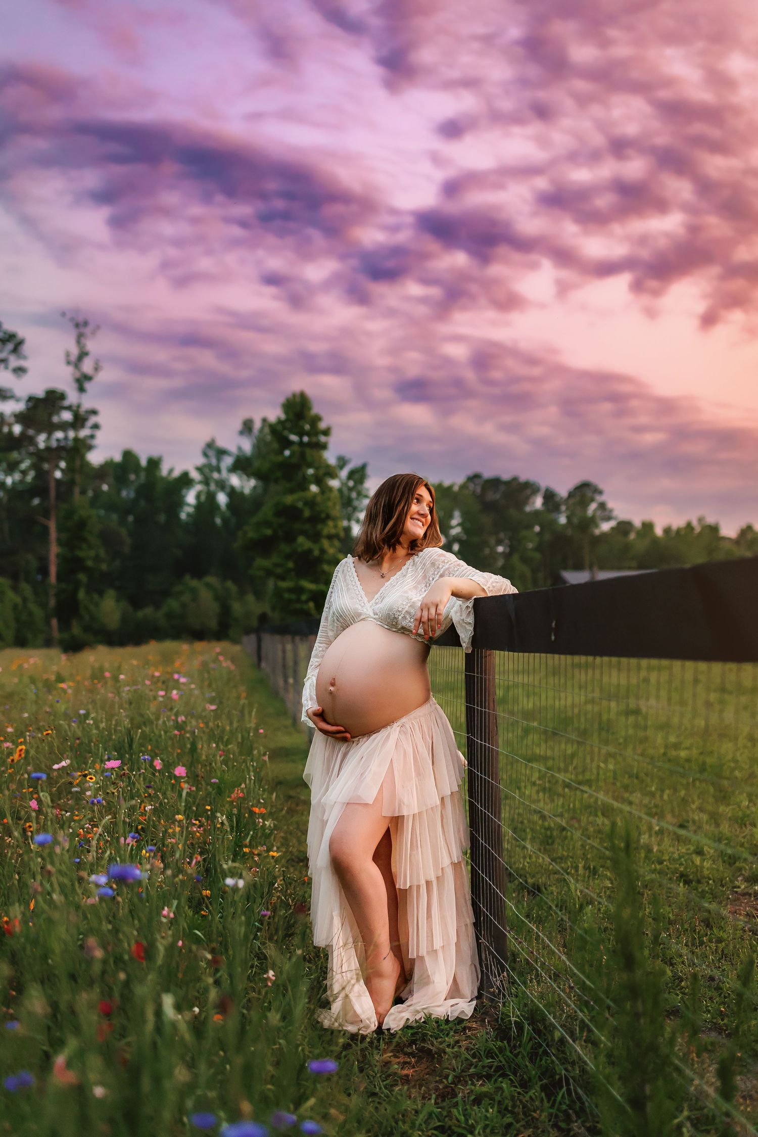 Maternity photo shoot in wildflower meadow at sunset with glowing pink and purple sky in background.