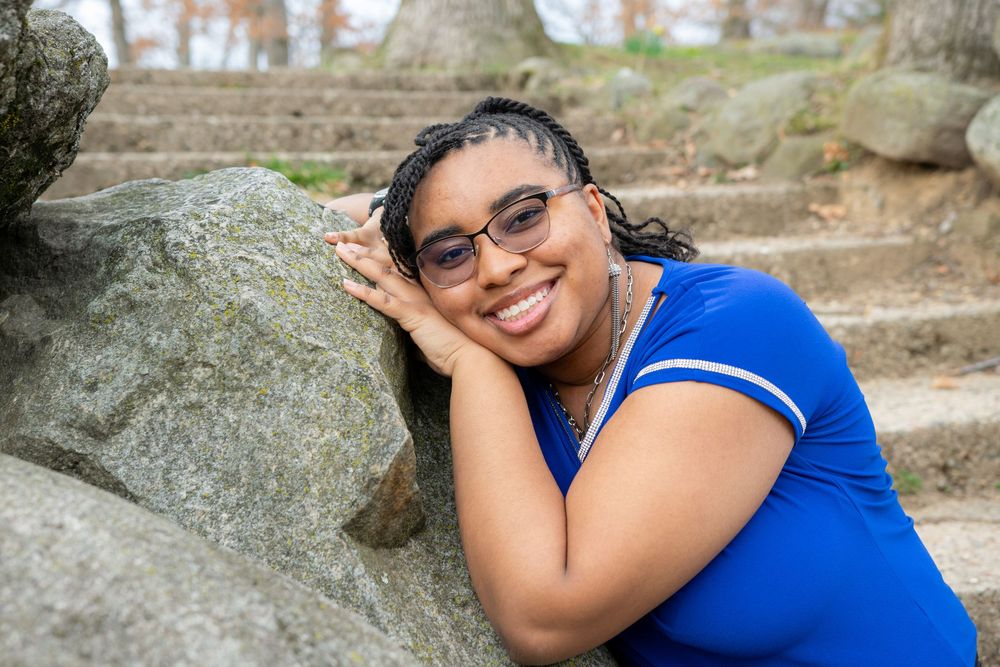 Person in blue shirt resting on rocky surface outdoors with trees in background.