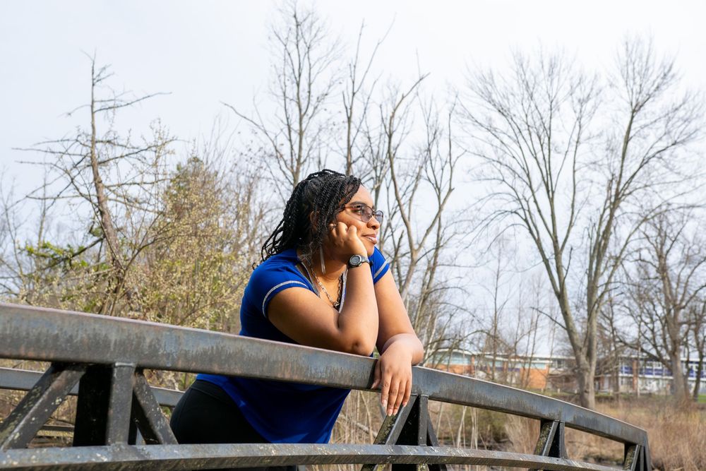 Person leaning on wooden railing with bare winter trees in background.