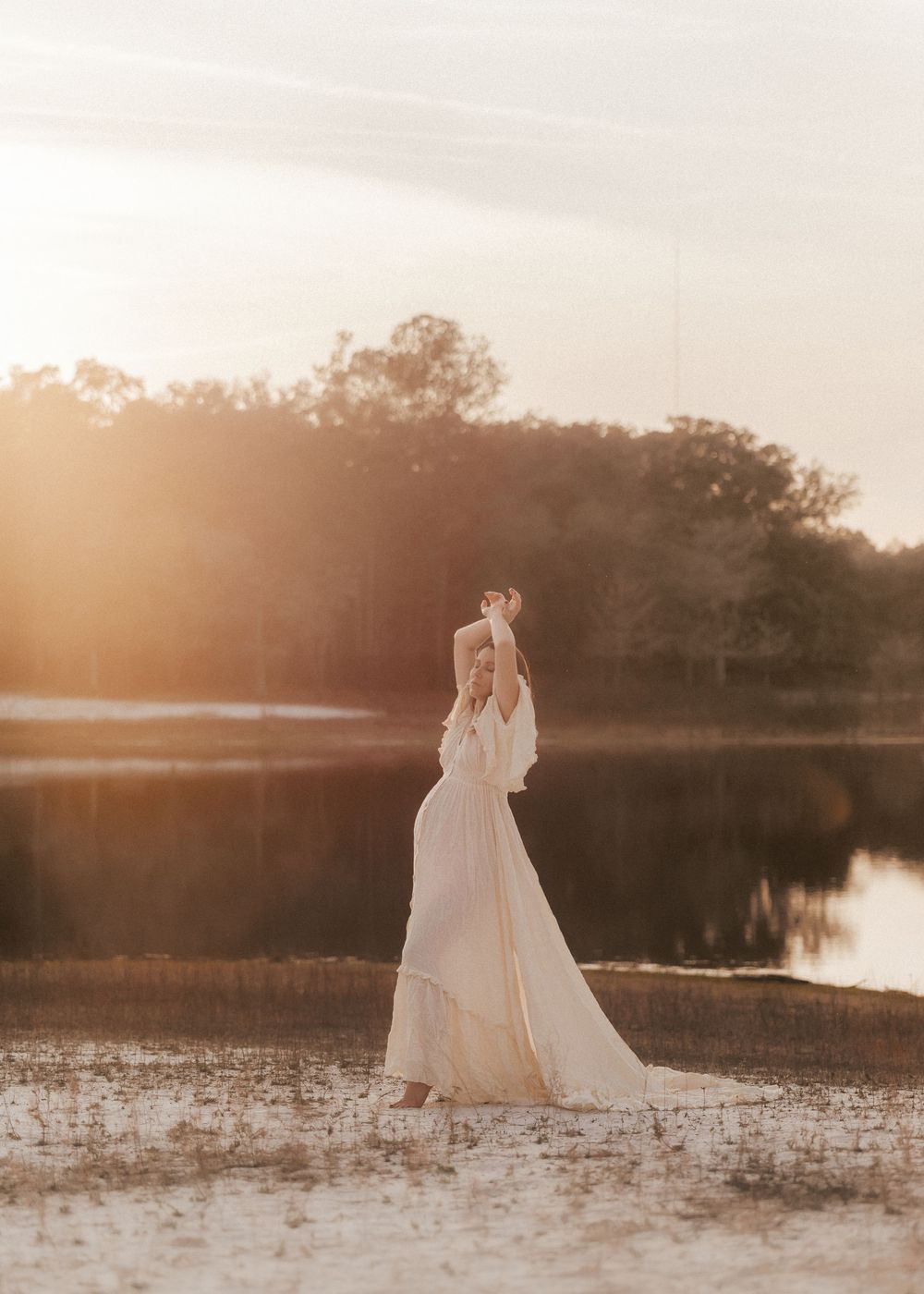 A bride in a flowing white dress walks through a misty lake at sunset creating a dreamy ethereal scene.