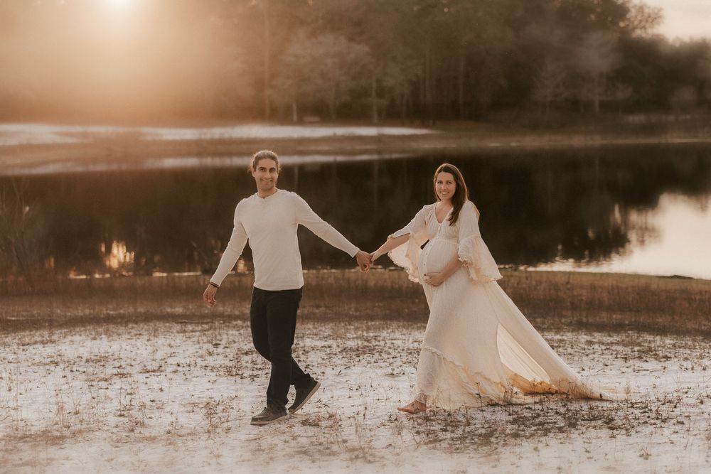 A couple in wedding attire dances and twirls together in a sunlit field at sunset creating a romantic silhouette.