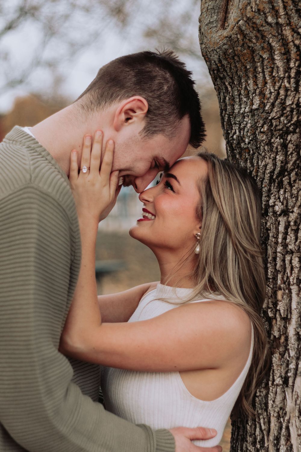 Romantic couple sharing a laugh while leaning against a tree trunk.