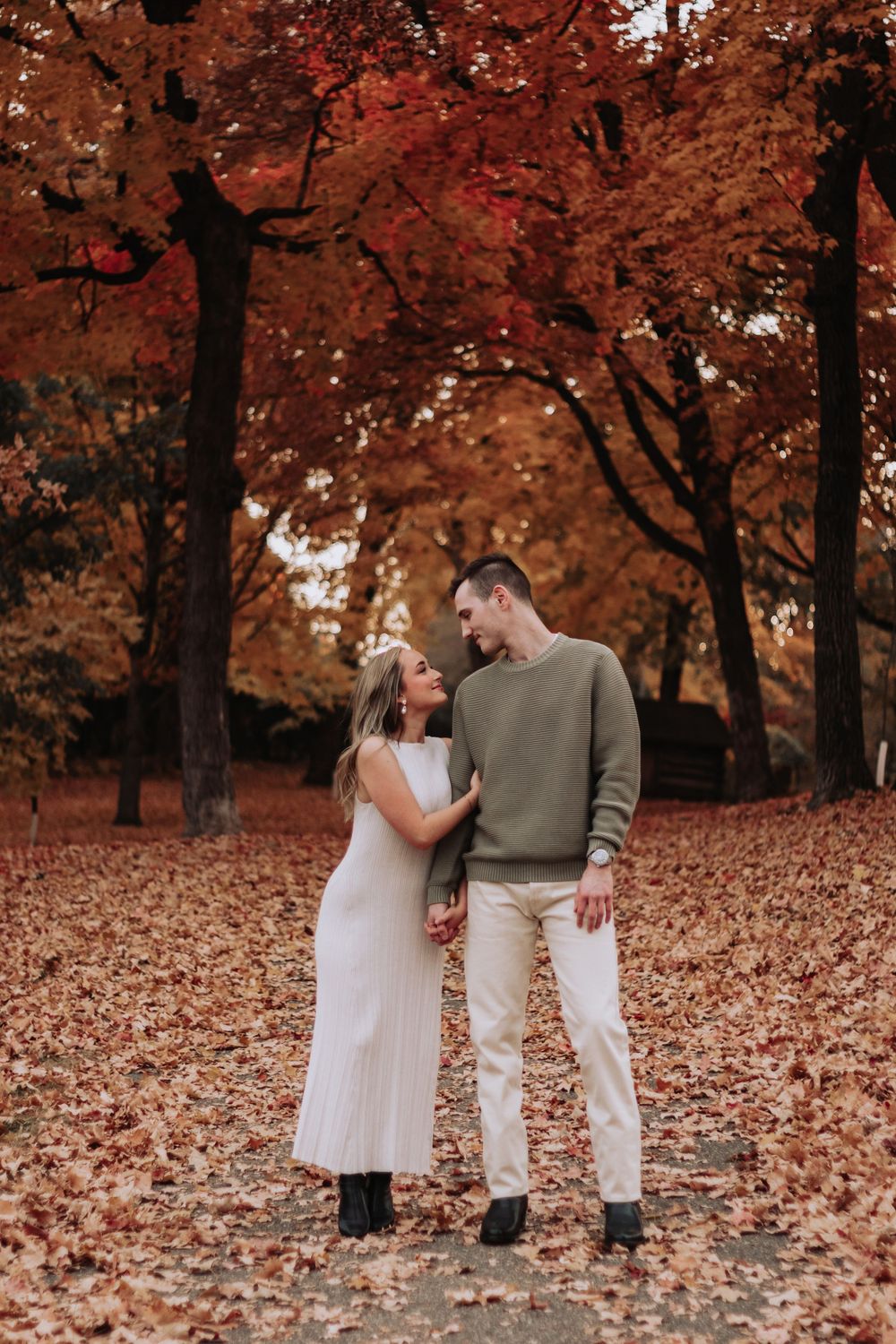 Couple in coordinated outfits standing among beautiful fall foliage.