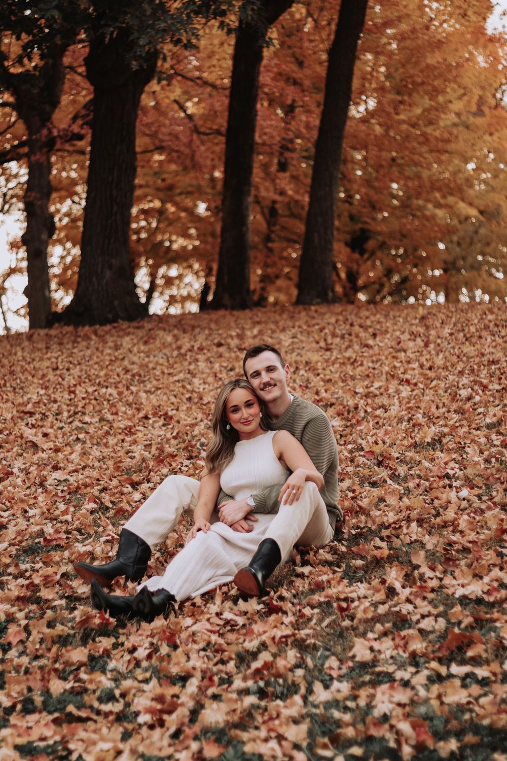 Couple sitting on autumn leaves enjoying a playful moment in the park.