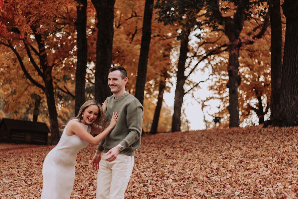 Joyful couple laughing while playing in fallen autumn leaves.