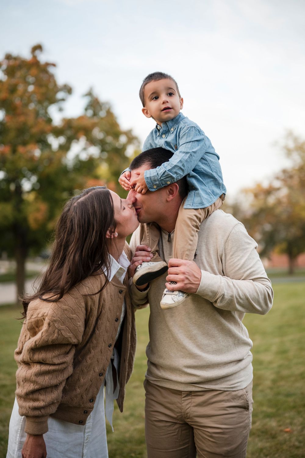A family shares tender moments together outdoors during an autumn photoshoot in a grassy field.
