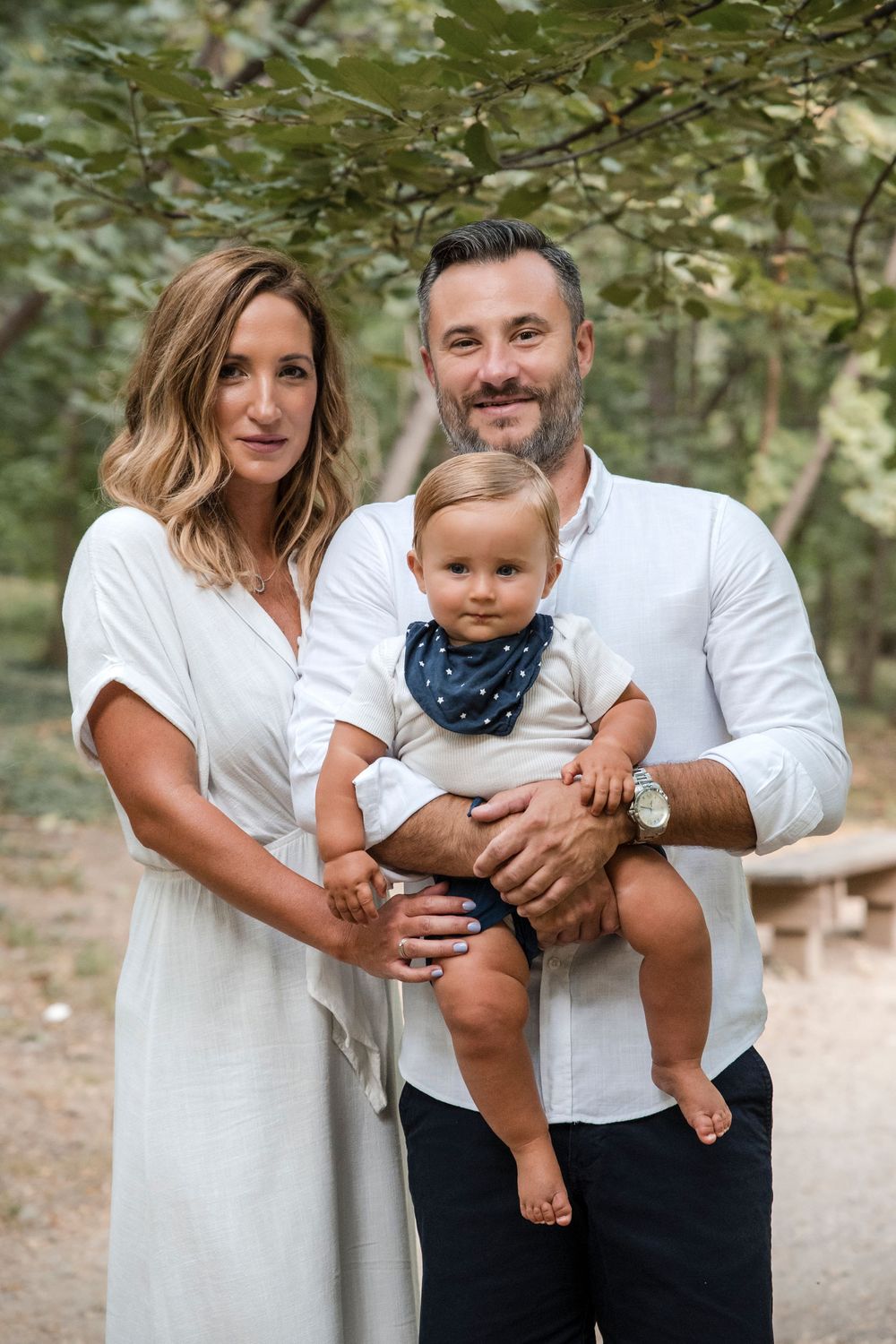 Family wearing white and black outfits poses together in an outdoor forest setting for a casual portrait session.
