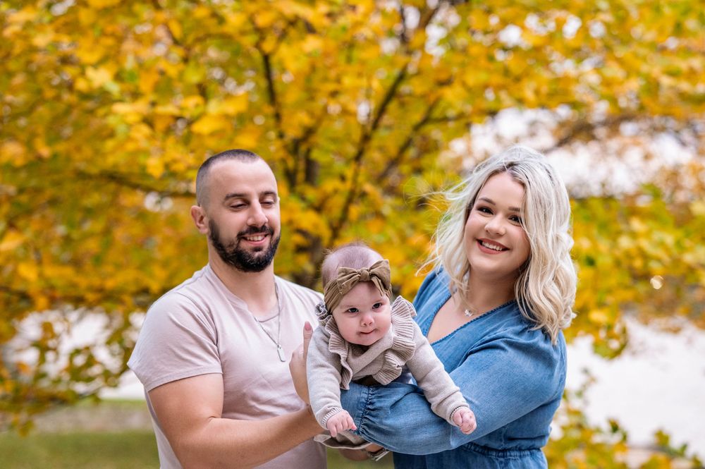 A family enjoys an autumn photoshoot together outdoors with golden yellow fall foliage in the background.