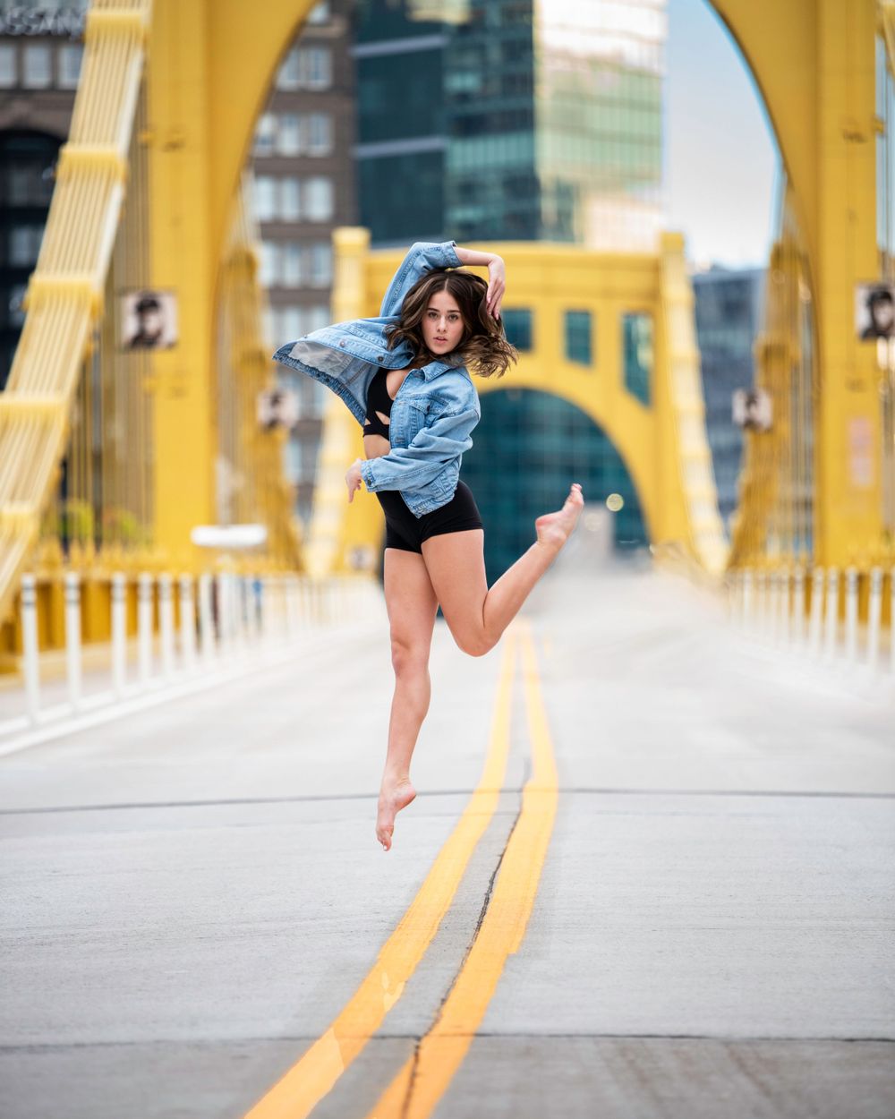A dancer in blue performs a graceful leap against yellow architectural pillars of the Sixth Street Bridge.