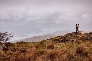 A person stands on a hilltop overlooking a scenic coastal landscape during golden hour.