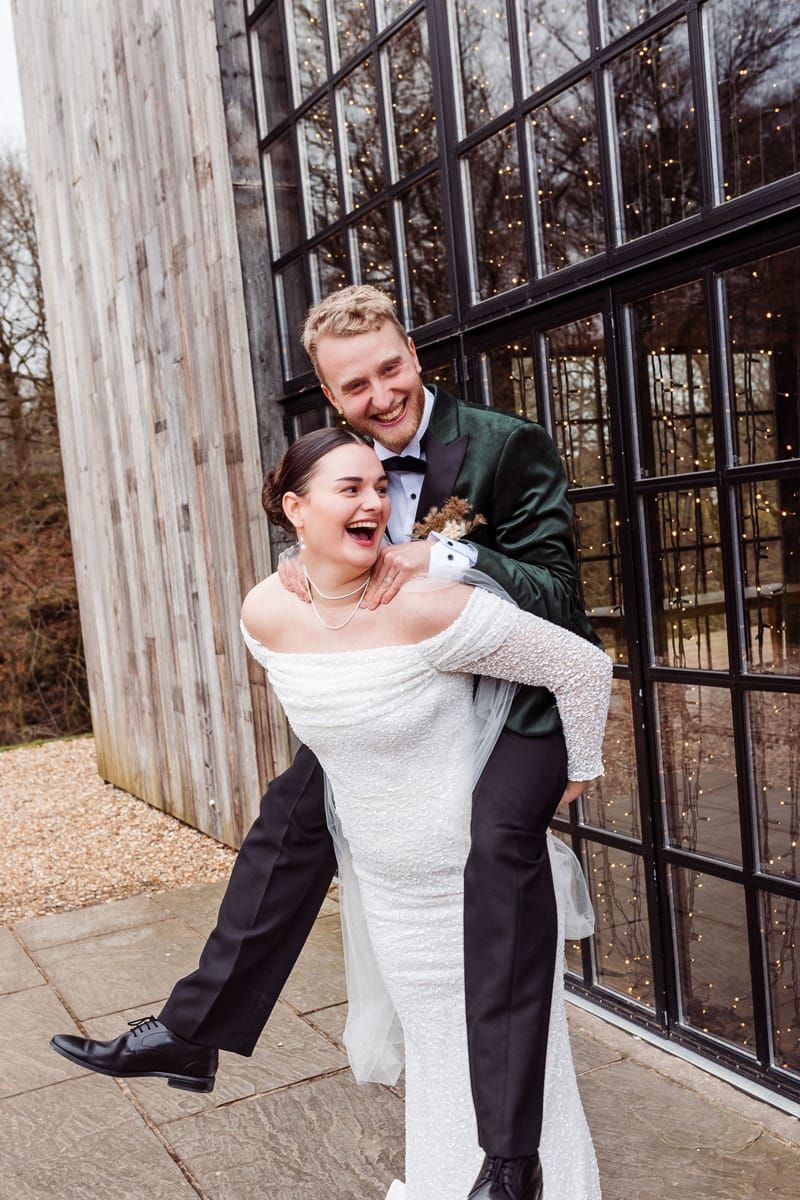 A newlywed couple shares a candid laughing moment together against a modern building exterior with large windows.