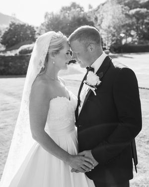 A black and white wedding photograph capturing an intimate moment between newlyweds on their special day outdoors.