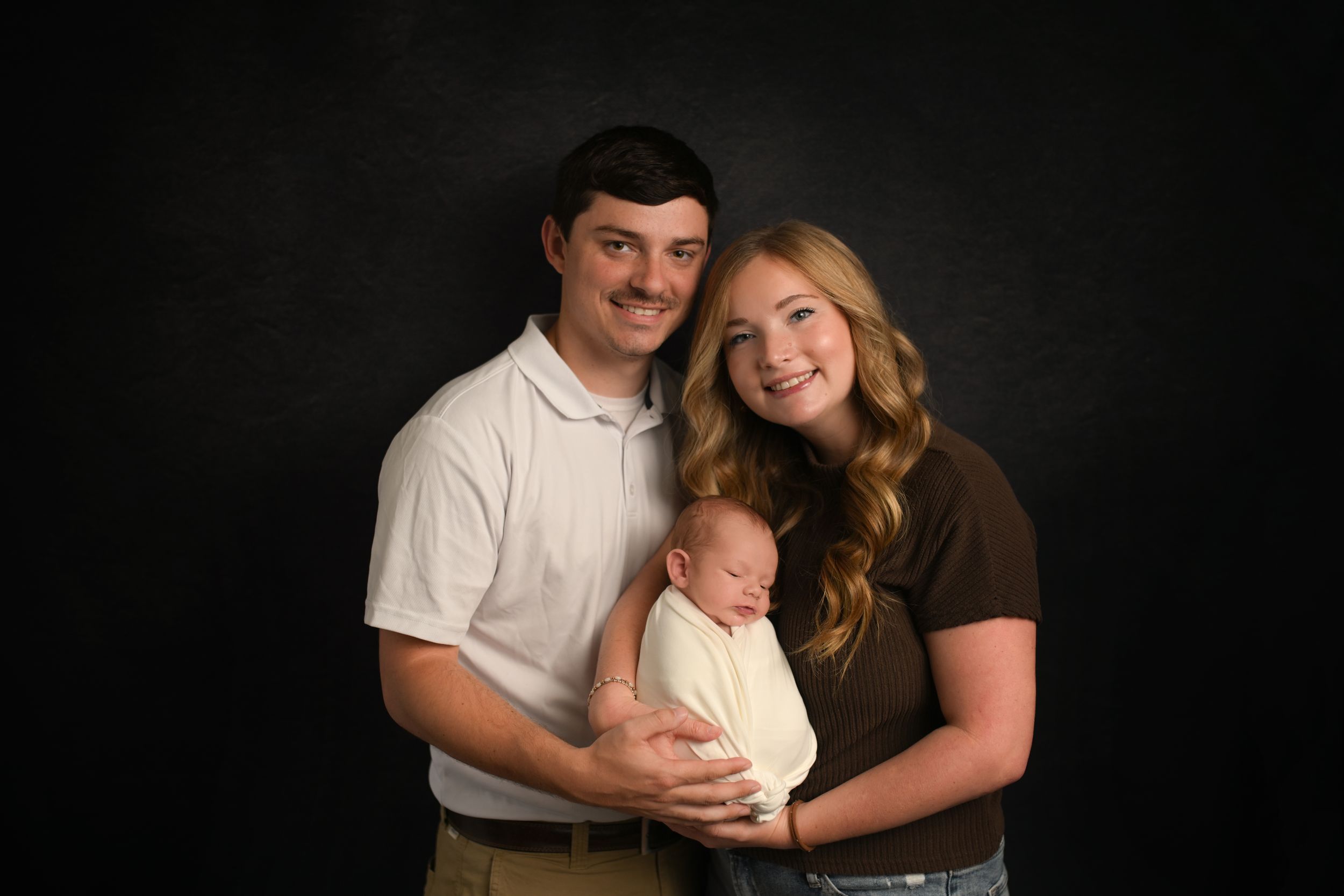 Professional family portrait on black background with dramatic lighting.
