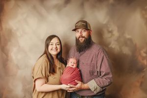 A heartwarming family photoshoot series with parents and baby in warm brown tones against a textured backdrop.