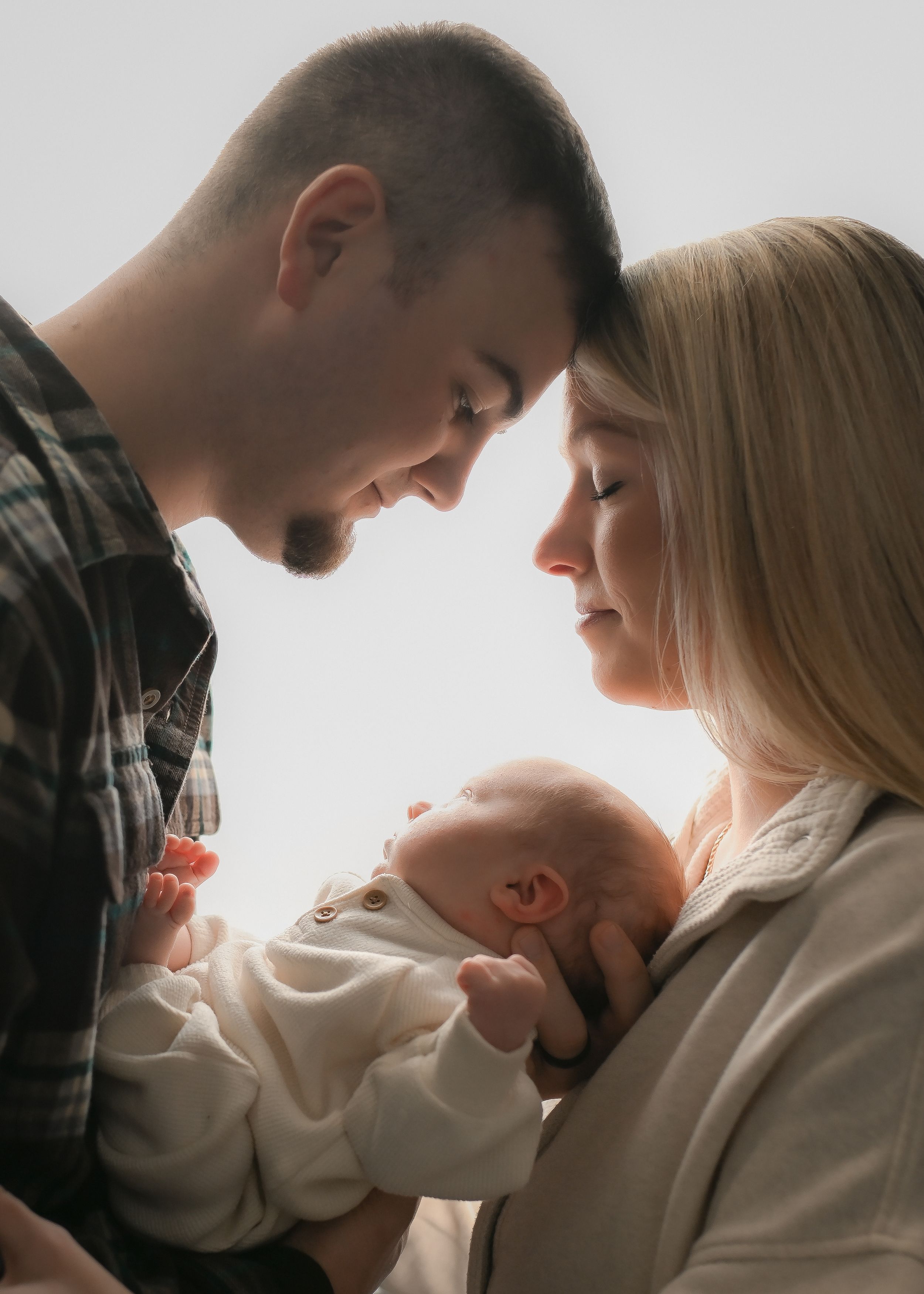 Gentle family moment captured as parents share tender moment with newborn in white clothing.