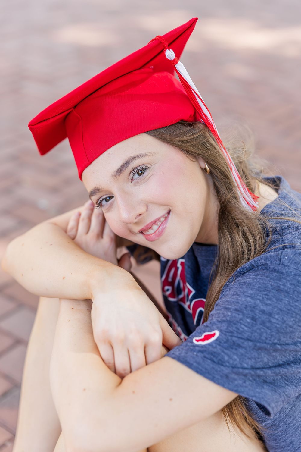 Graduate in red cap and navy sweater poses with natural smile during outdoor photo session.