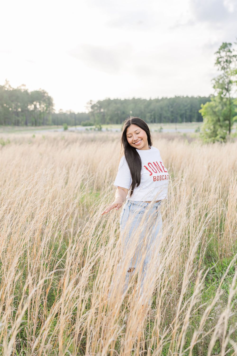 A person in a white t-shirt poses playfully in a tall grass field on a sunny day.