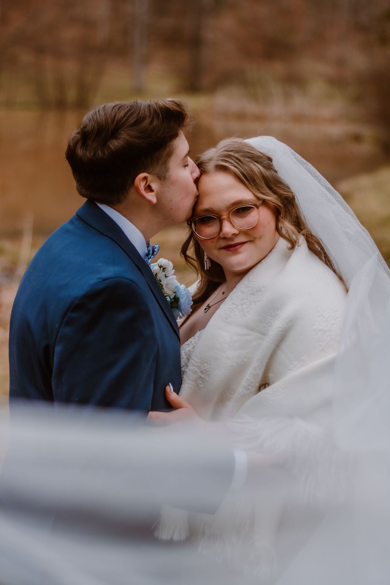 A winter wedding couple shares a tender moment wrapped in a white fur shawl.