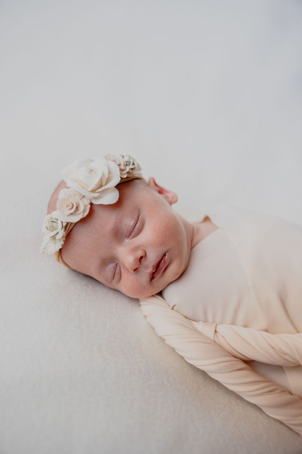 Sleeping newborn wearing delicate floral headband against light background in studio in Oostburg, WI  with Essence Rose Photography.