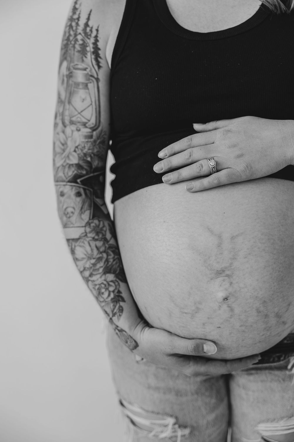Black and white maternity photo showing tattooed arms cradling a pregnant belly in Milwaukee, WI  with Essence Rose Photography.
