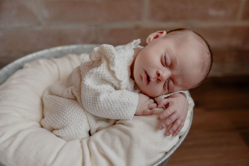 Sleeping newborn wrapped in white knit blanket on wooden surface in Oostburg, WI  with Essence Rose Photography.