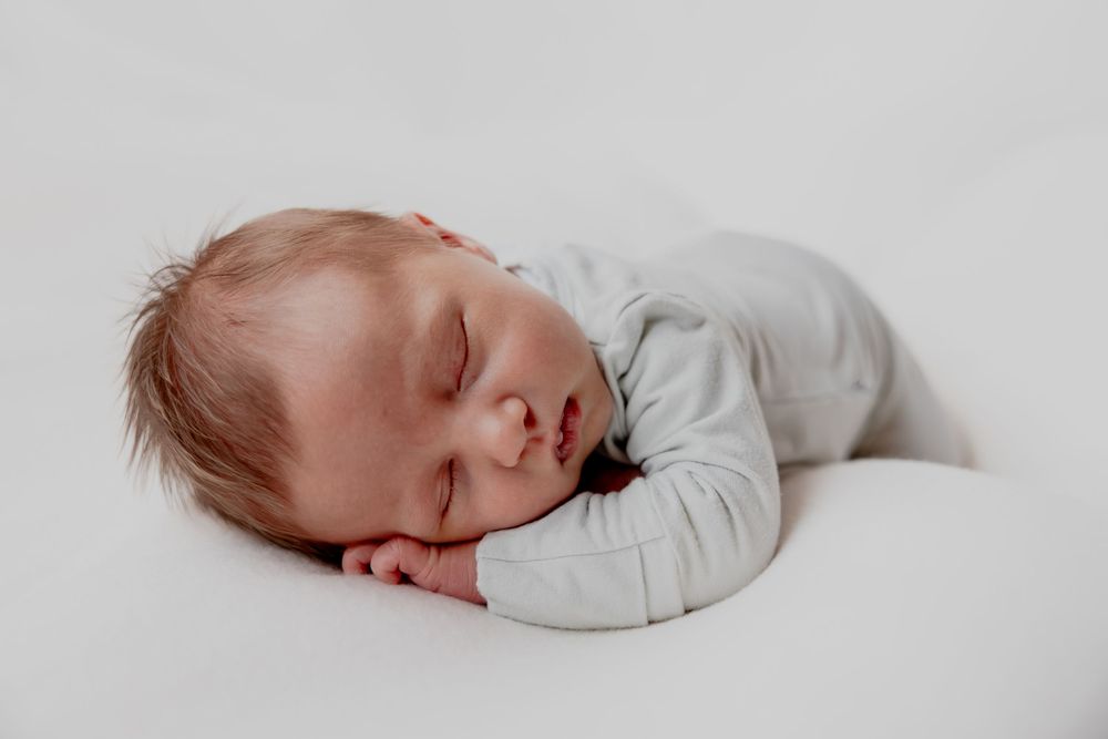 Peaceful sleeping newborn in light gray clothing against white background in Oostburg, WI studio  with Essence Rose Photography.