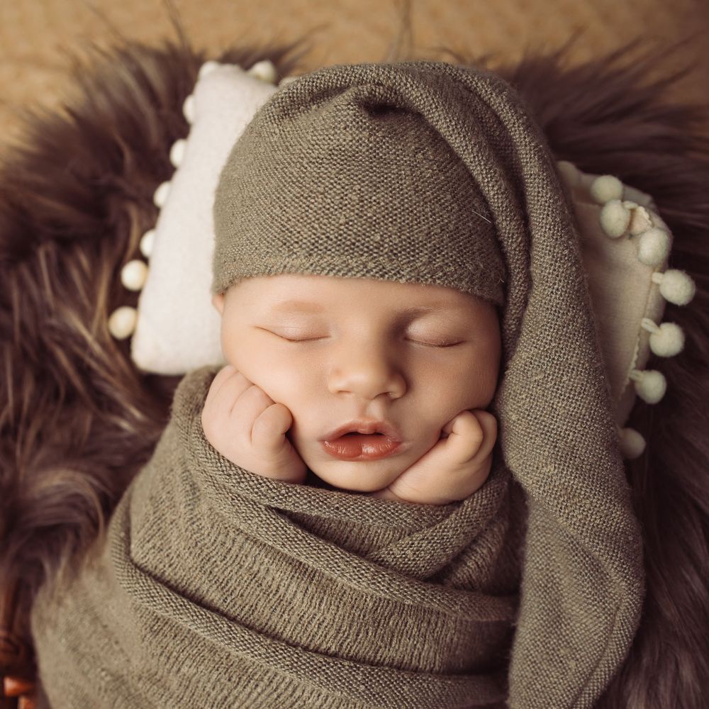Newborn baby swaddled in soft brown knit fabric with delicate lighting creating a cozy sleeping portrait.