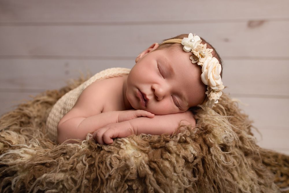A sleeping newborn baby lies peacefully on soft brown fur during a professional photo session.
