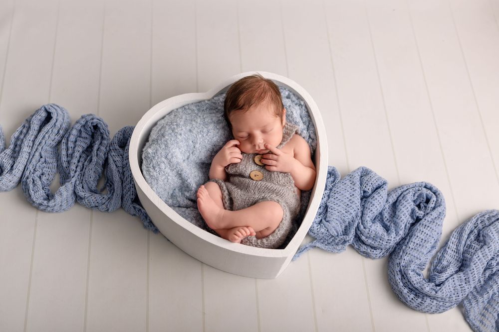 A sleeping newborn baby curled up in a white bowl with soft blue knitted fabric surrounding them.