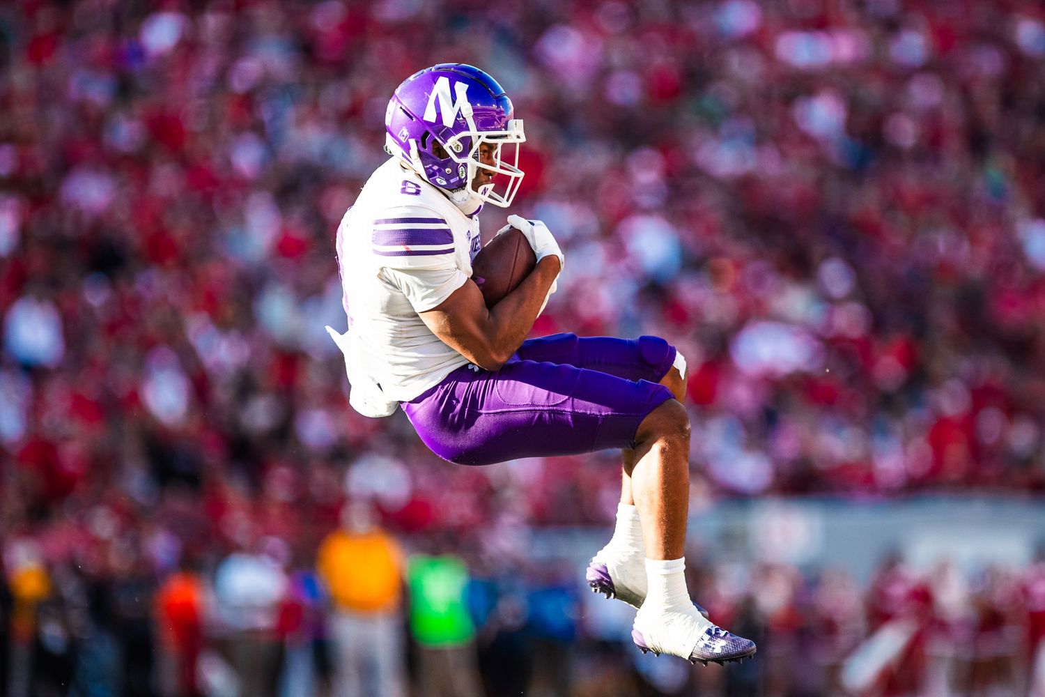 Football players in purple and white uniforms competing during an intense game at a packed stadium.