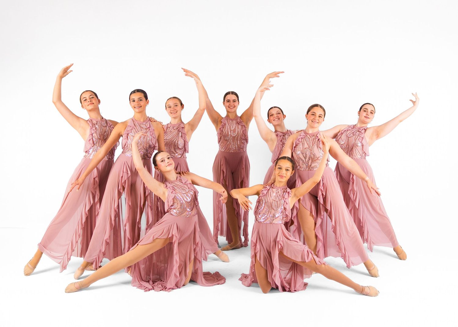 Professional dance group in white costumes with red and blue sashes posing in formation on studio floor.