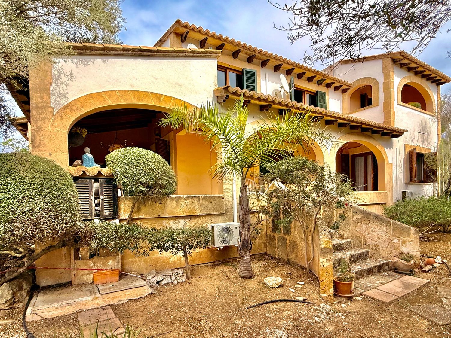 Rustic stone terrace with wooden benches and potted plants in Mediterranean garden.